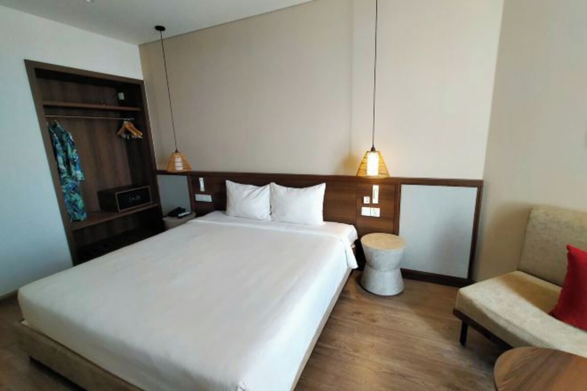 Una habitación de hotel con una cama grande, una mesita de noche y una zona de estar con una silla.