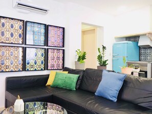 Un salon avec un canapé en cuir noir, des coussins colorés, une table basse en verre et un mur décoré de carreaux à motifs.