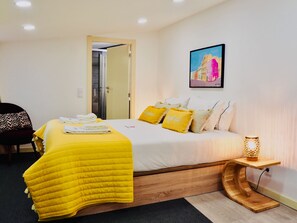 Une chambre d’hôtel comprenant un lit, une table de chevet avec une lampe, une chaise et une porte donnant sur une salle de bain.
