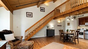 Un vaste salon agrémenté d’un escalier en bois, un coin repas avec des meubles en bois et une cuisine équipée d’appareils électroménagers modernes.