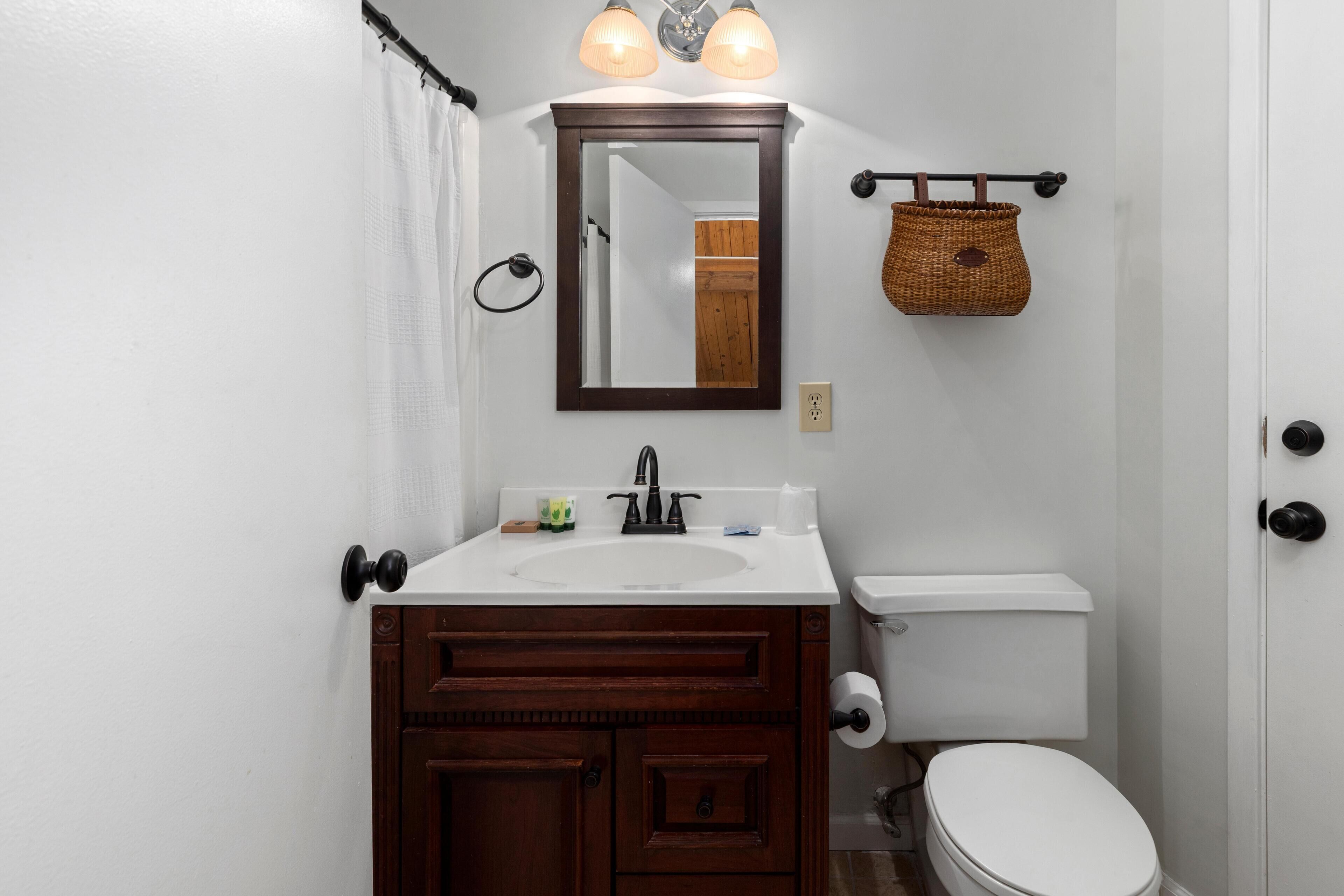A bathroom with a white sink, dark wooden vanity, a white toilet, and a mirror above the sink.