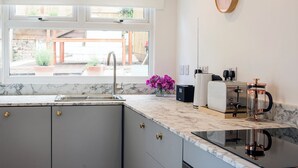 A modern kitchen with a marble countertop, a sink, a coffee maker, and a window with a view of the outside. - Cornish Cottage - Truro City Centre (Truro)