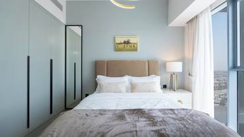 A modern hotel room with a large bed, a headboard, a bedside table with a lamp, a framed picture on the wall, and a view of the city through the window.