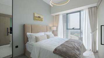 A modern bedroom with a large bed, a bedside table, a mirror, and a view of the city through a large window.