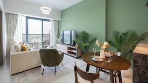 A modern living room with a sofa, a dining table set, a TV, and large windows. - KeyRock Golf Gate - Stylish Retreat (Dubai)