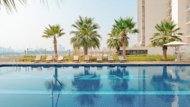 A swimming pool with lounge chairs and palm trees, surrounded by a modern building with balconies. - KeyRock Golf Gate - Stylish Retreat (Dubai)