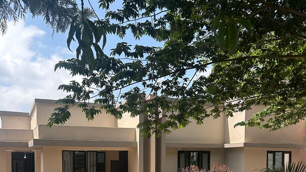 A building with a flat roof, multiple windows, and a paved entrance area with two chairs. - Victorious Chillzone Hostel (Arusha)