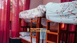 A bunk bed room with a floral bedspread, a small rug, and a window with pink curtains. - Victorious Chillzone Hostel (Arusha)