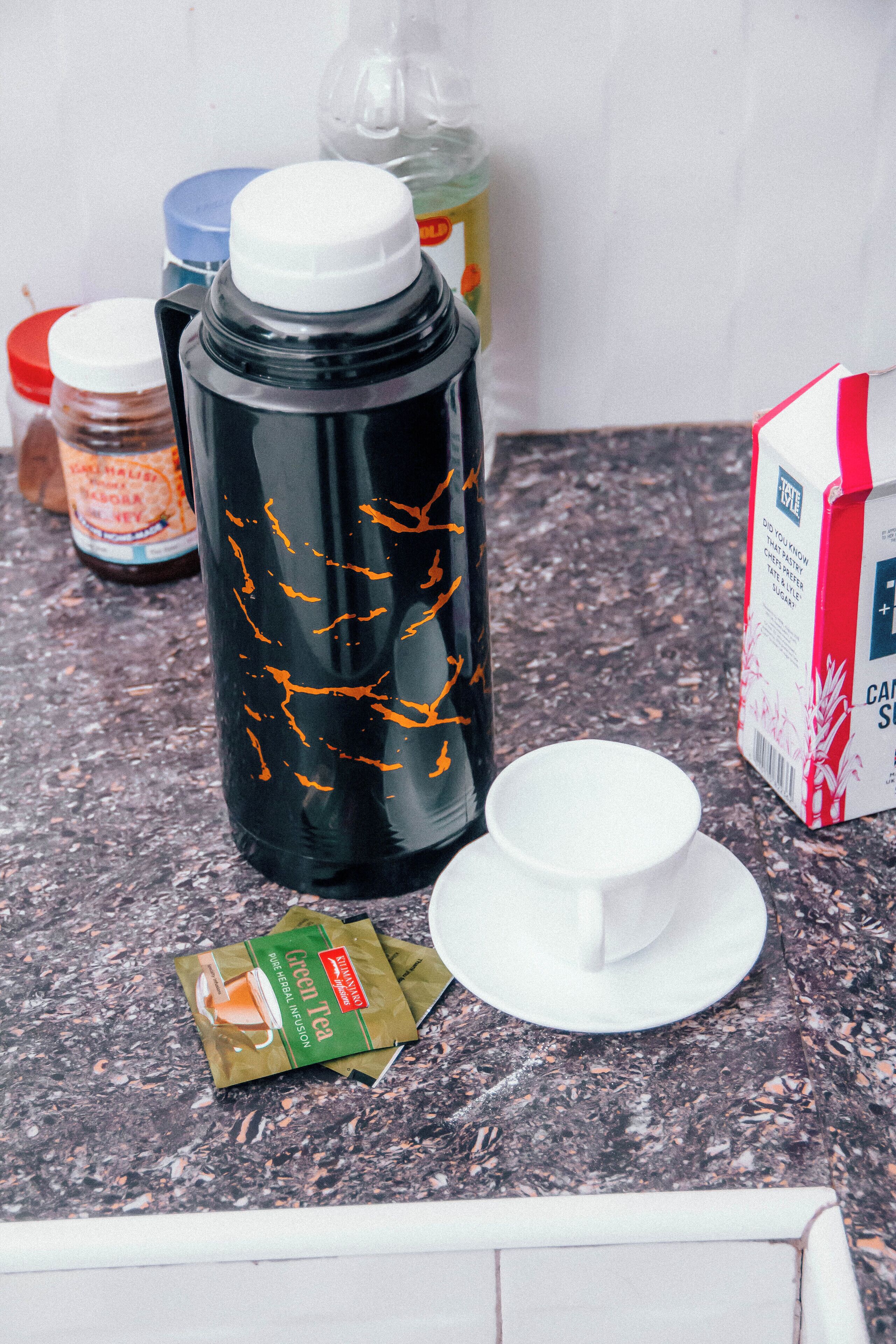 A kitchen counter with a coffee maker, a packet of green tea, a milk carton, and a jar of spices.