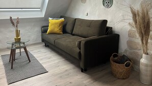 Un salón estilo loft con un sofá marrón, un cojín amarillo, una mesa de centro de vidrio, una alfombra estampada y una pared de piedra decorada con platos.