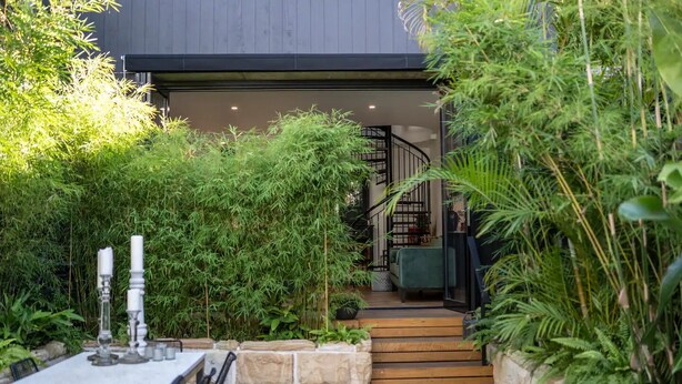 A modern outdoor patio with a dining table and chairs, surrounded by lush greenery and a staircase leading to an upper level. - UNIQUE- Boutique Designer - The Barn Paddington (Sydney)
