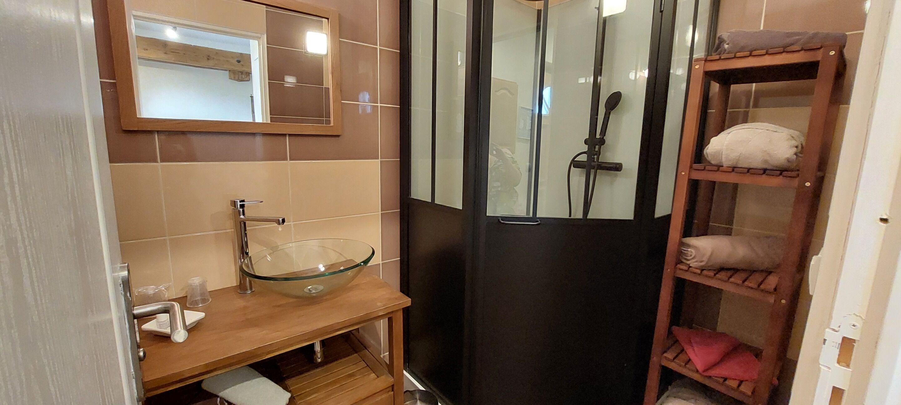 Un baño con lavamanos de vidrio, tocador de madera, espejo y cabina de ducha.