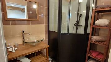 Un baño con lavamanos de vidrio, tocador de madera, espejo y cabina de ducha.