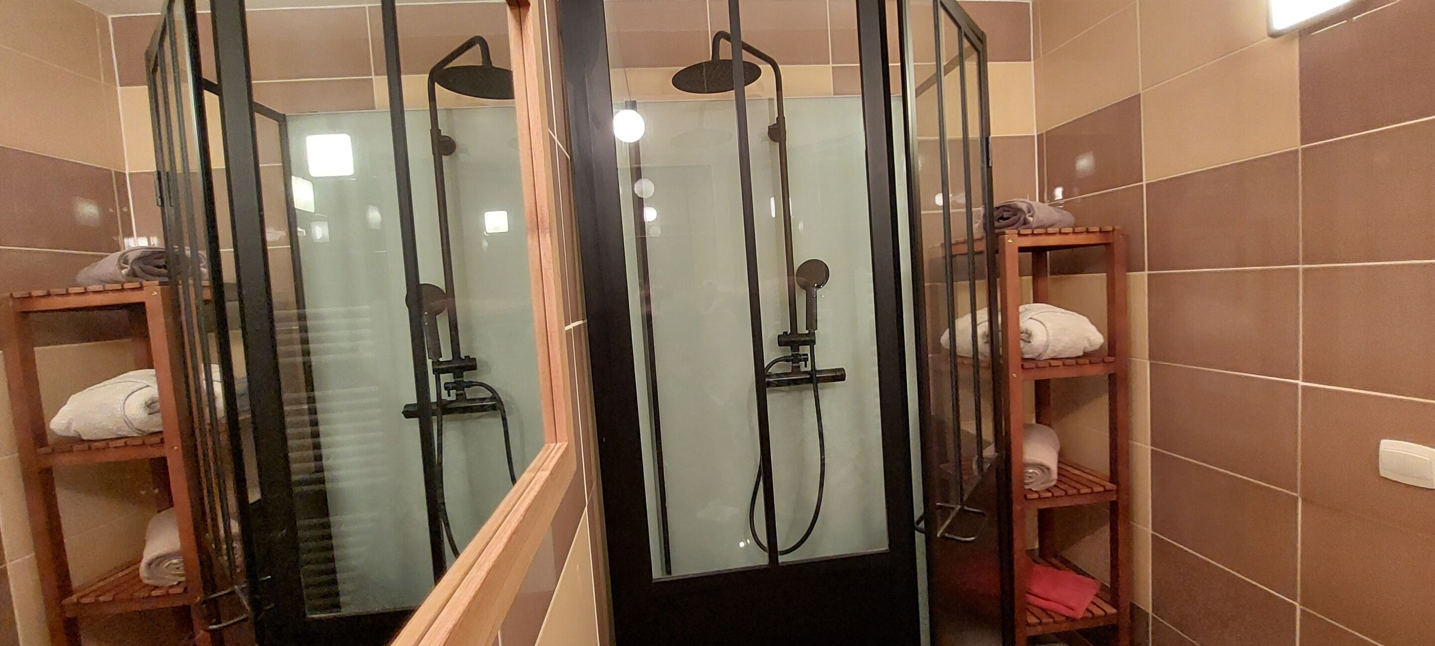 Un espacio de ducha con puertas de vidrio, repisas de madera con toallas y un revestimiento de azulejos.