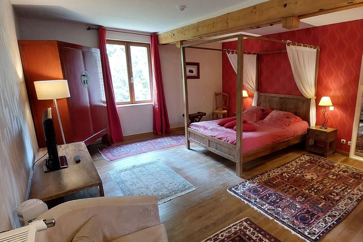 Un lit à baldaquin, une armoire en bois, un bureau avec une lampe et un grand miroir.