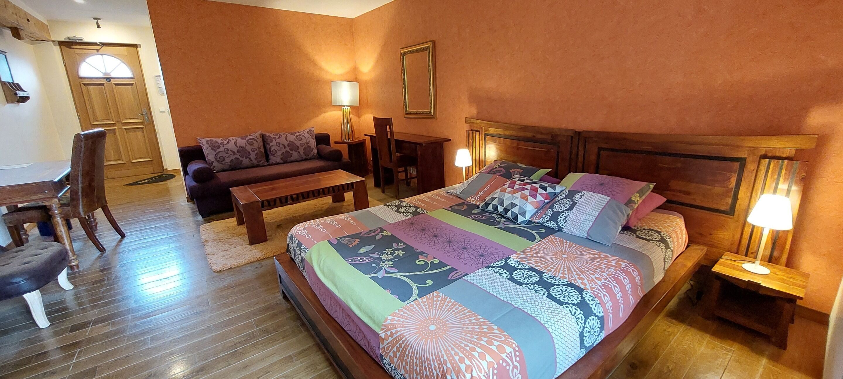 Habitación de hotel con una cama grande, un sofá, una mesa de centro de madera, una mesa de comedor y sillas.
