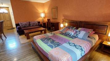 Habitación de hotel con una cama grande, un sofá, una mesa de centro de madera, una mesa de comedor y sillas.