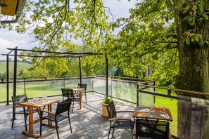 Een terras buiten met tafels en stoelen, met uitzicht op een weelderig groen landschap.
