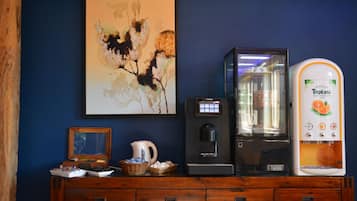 Una cafetera, una obra de arte enmarco y una jarra de café sobre un mueble de madera.