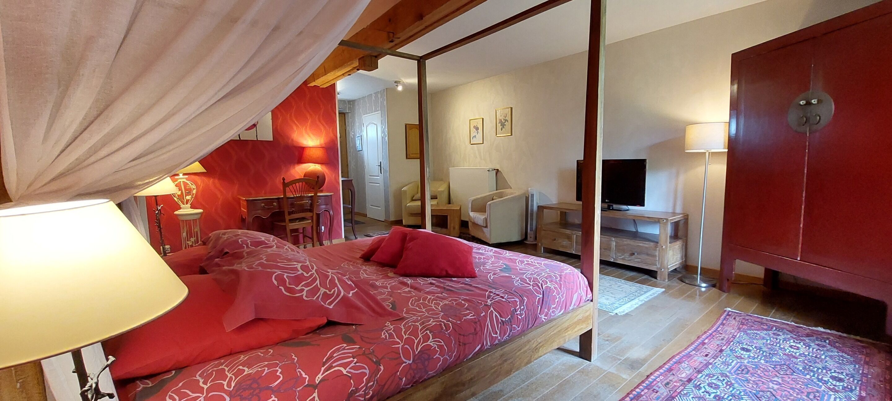 Un dormitorio con cama con dosel, un escritorio, una silla, un televisor y un armario.