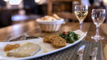 Un tavolo da pranzo con un piatto di cibo, due bicchieri di vino bianco e un cestino di pane.