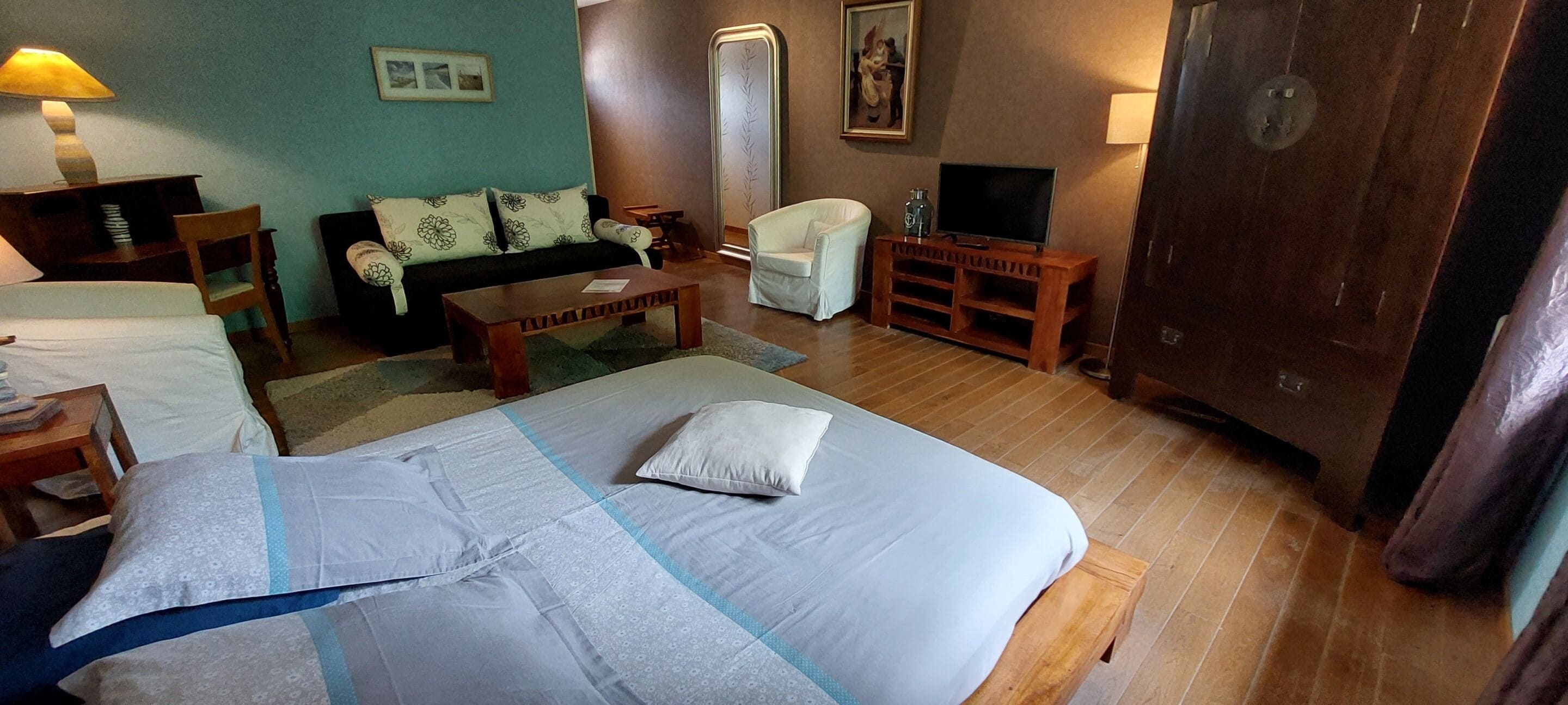 A hotel room with a bed, a sofa, a chair, a TV stand, and a desk.