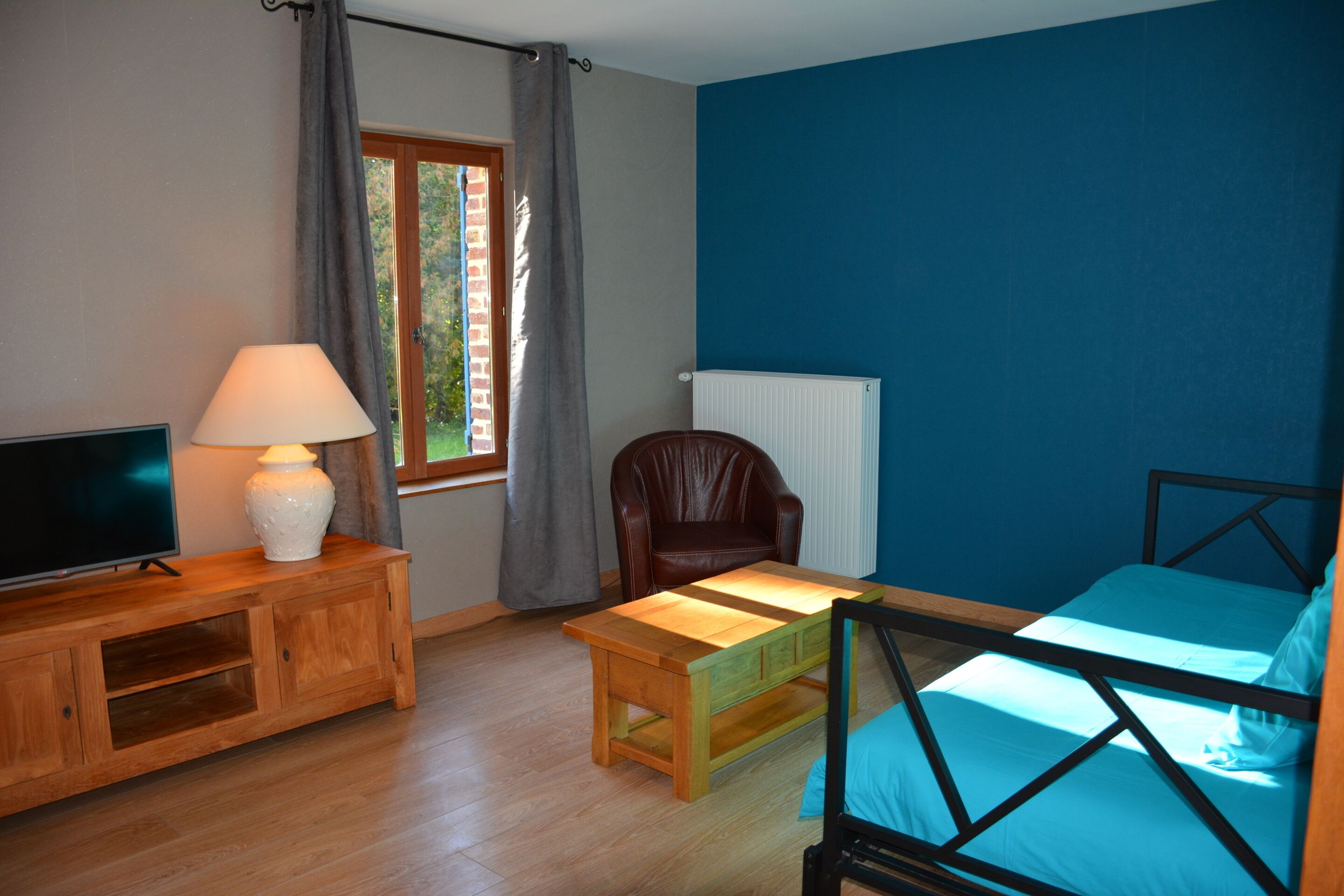Een kamer met een bed, een televisie op een houten kast, een stoel, een tafel en een raam met gordijnen.