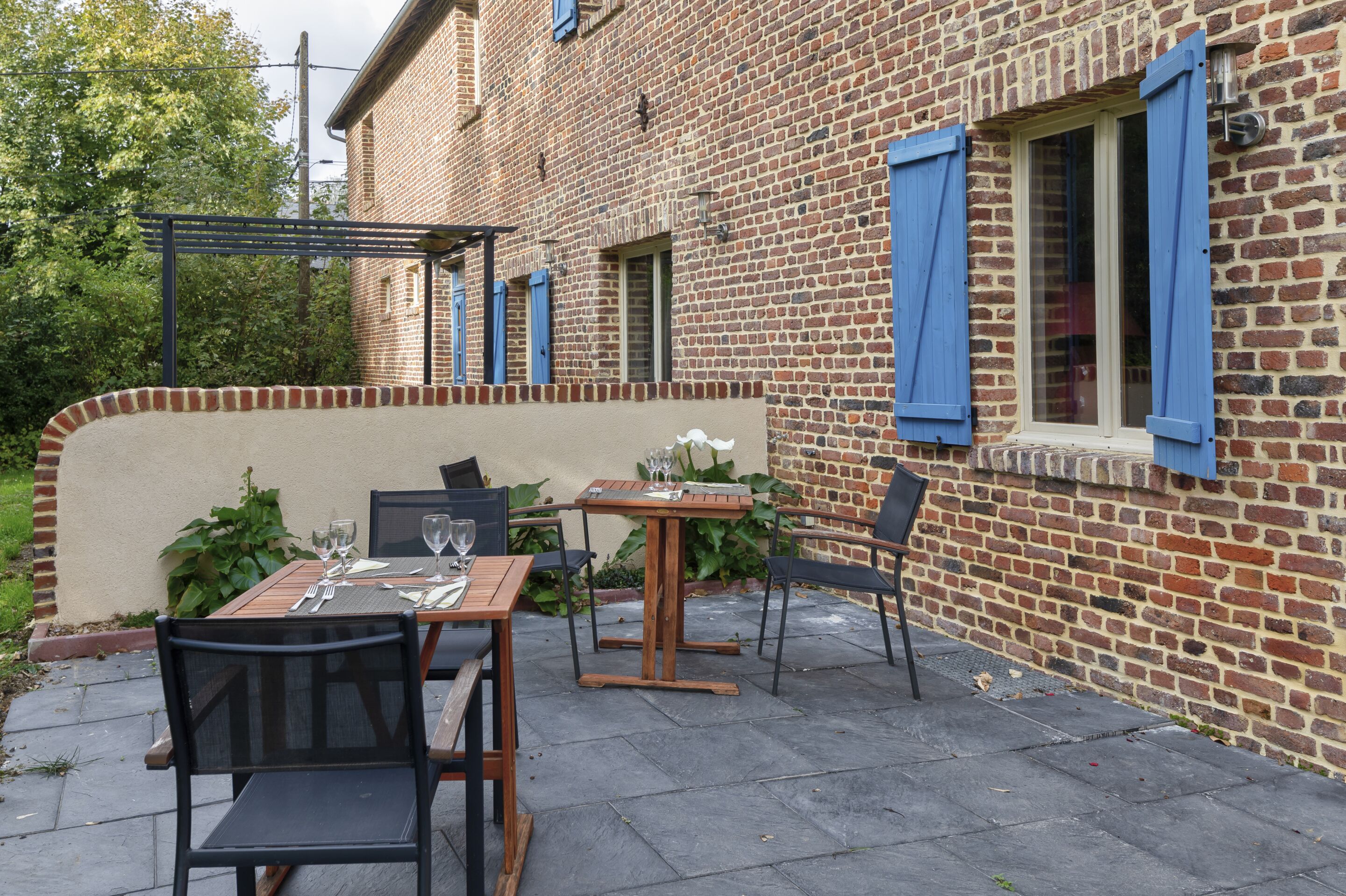 An outdoor patio with a brick wall, wooden tables, and chairs.