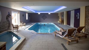 Piscina interna com uma pessoa nadando, cadeiras de descanso e uma pequena área de estar.