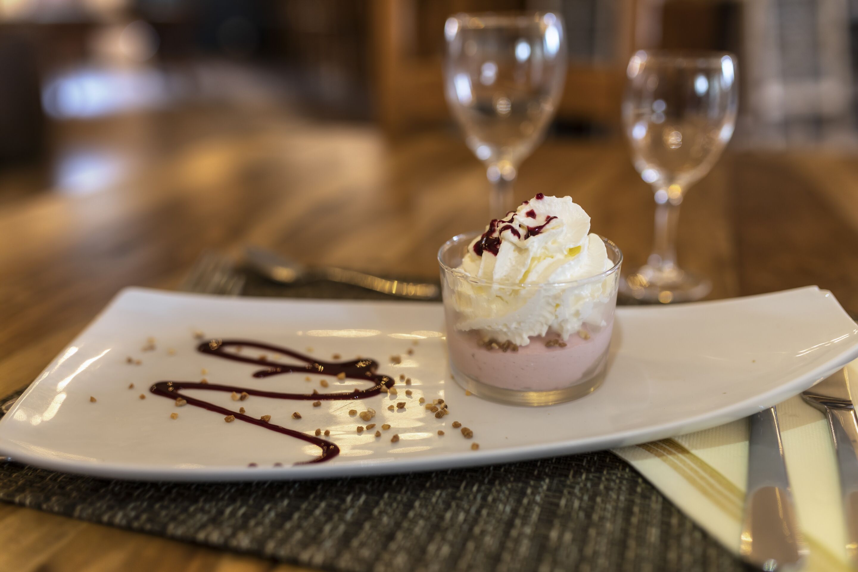 A dessert on a white plate with chocolate sauce and nuts, accompanied by a fork and knife on a placemat.