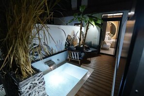 A modern spa area with a large bathtub, wooden deck, and seating area with a view into a bedroom. - Barneys Club B&b (Cercola)