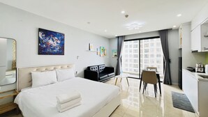Une chambre d’hôtel avec un grand lit, un bureau, une chaise, une kitchenette et une vue sur la ville par la fenêtre.