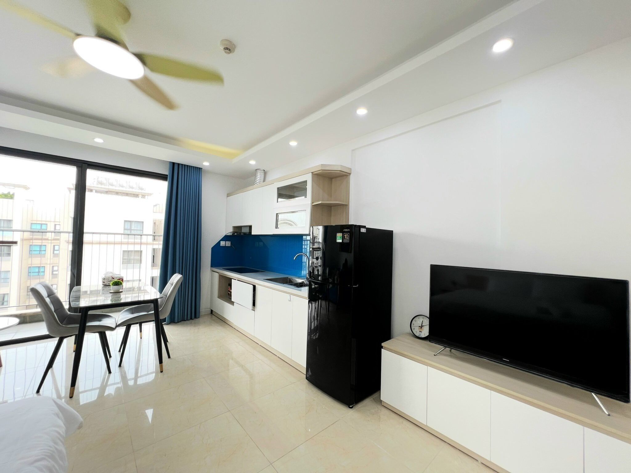 Una cocina moderna con un refrigerador negro, un salpicadero azul y un televisor de pantalla plana sobre un mueble de madera.