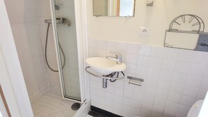 Un baño con ducha de vidrio, un lavabo blanco con grifo cromado y un espejo sobre el lavabo.