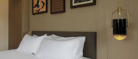 A hotel room with a neatly made bed, framed artwork on the wall, and a modern light fixture.