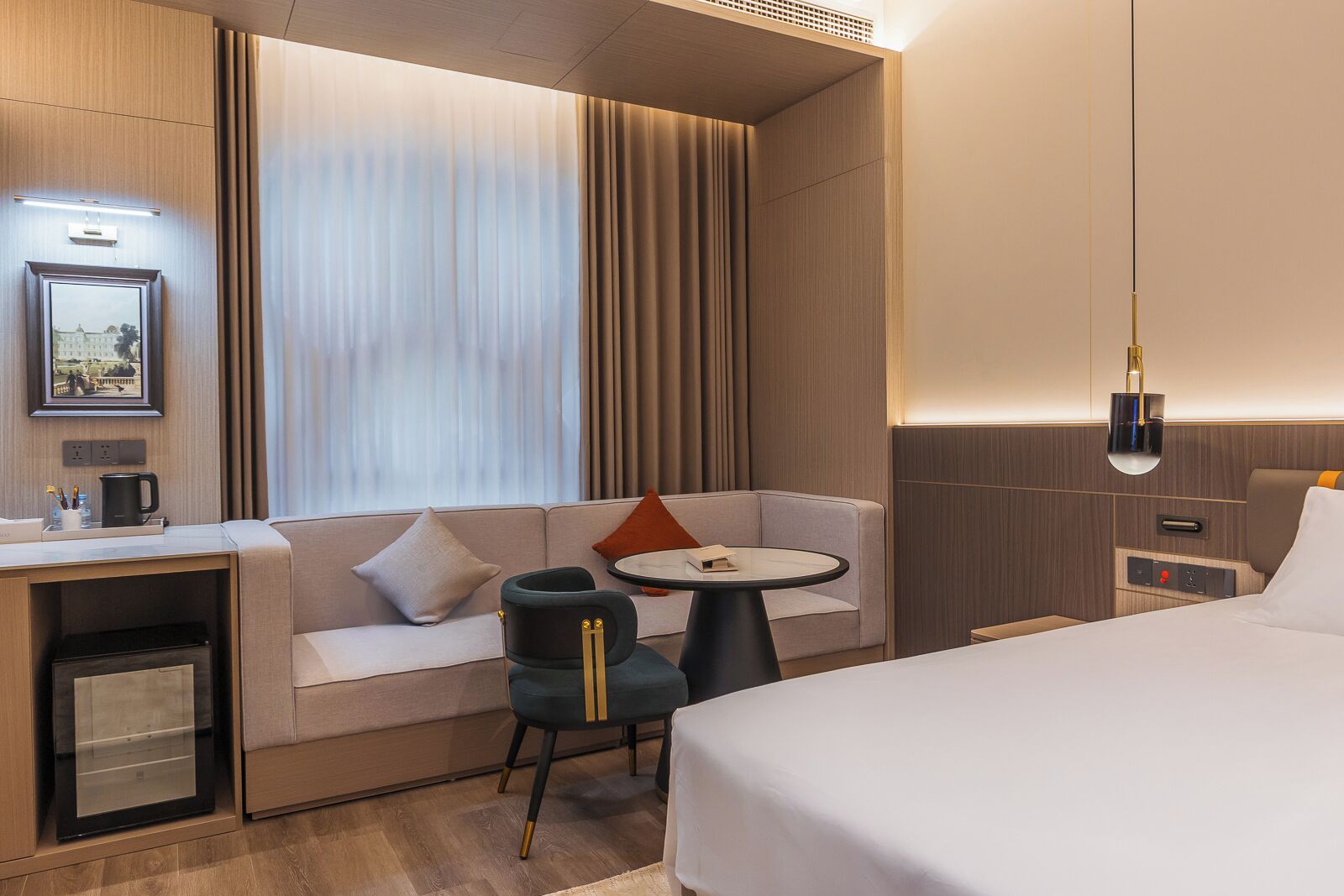 A modern hotel room with a bed, a sofa, a small table, a desk with a coffee machine, and a TV.
