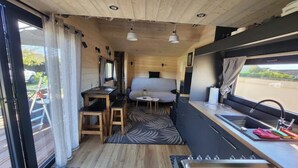 Interior compacto de autocaravana con kitchenette, un pequeño comedor y una cama.