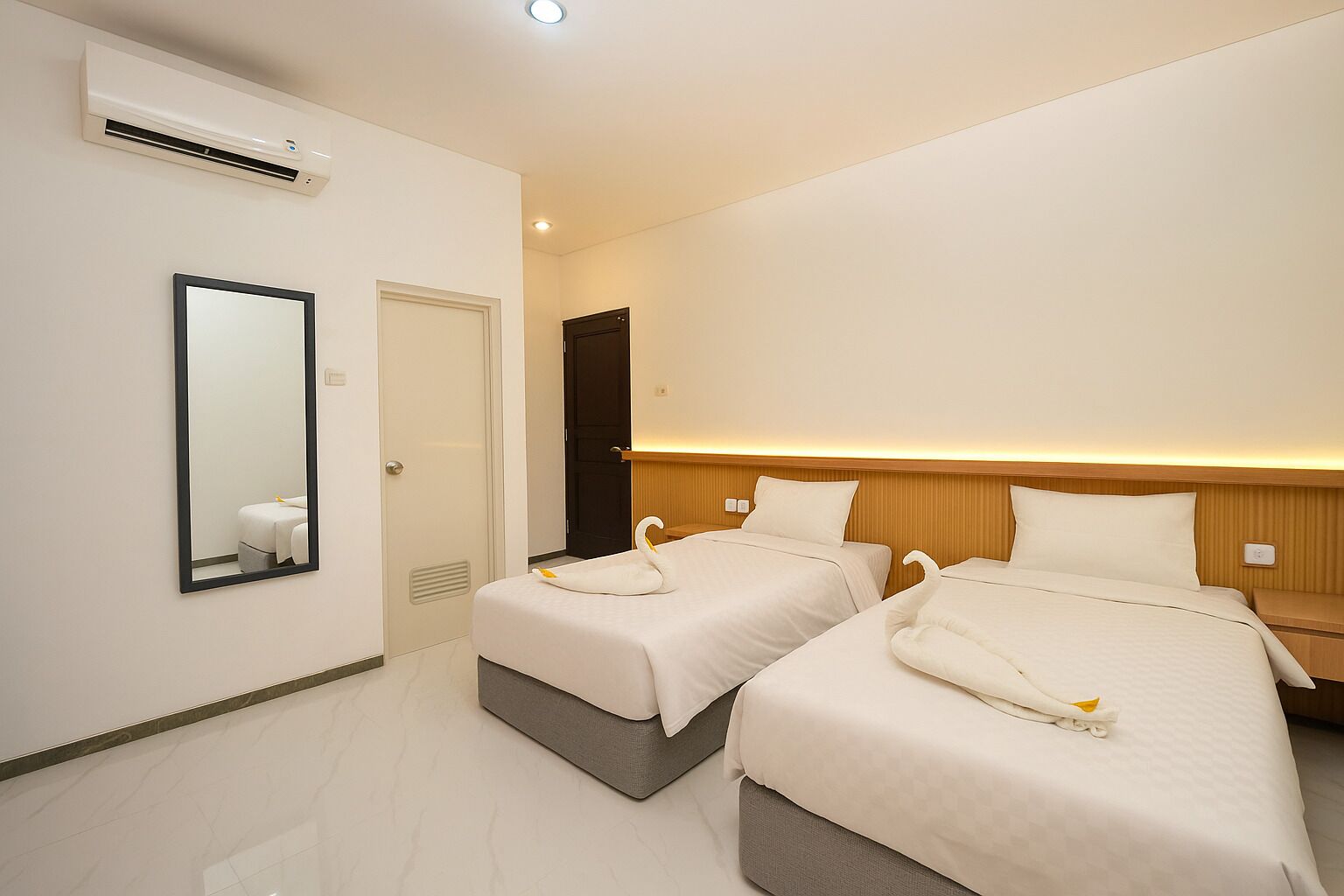A hotel room with two beds, a mirror, an air conditioning unit, and a door.