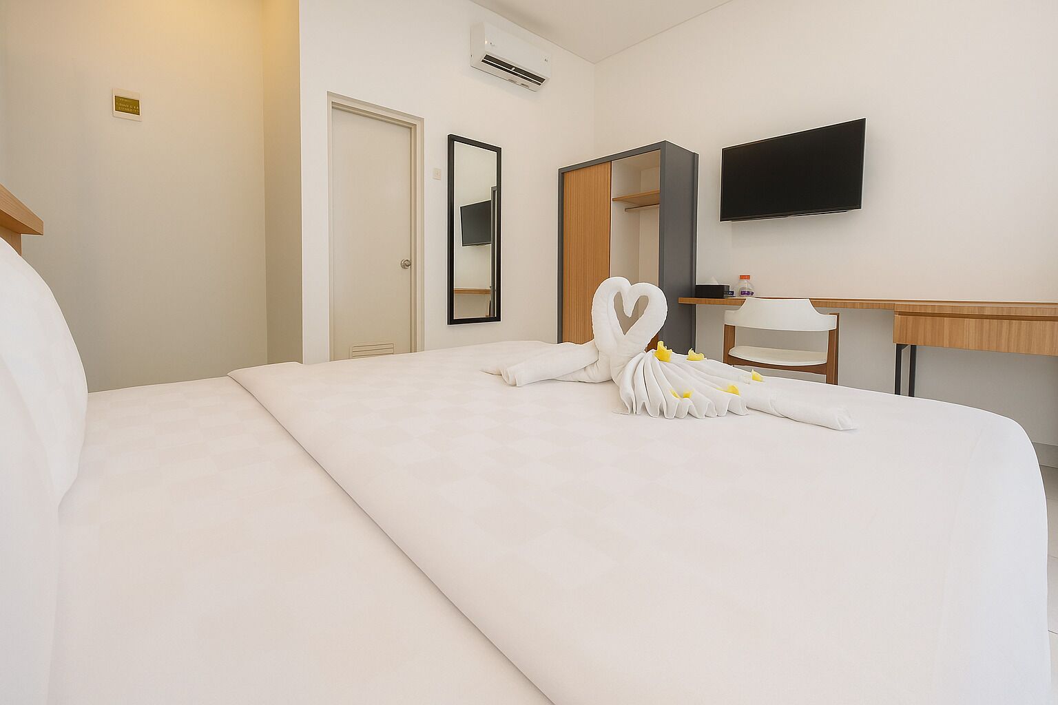 A hotel room with a large bed, a desk, a chair, a flat-screen TV, and a mirror.