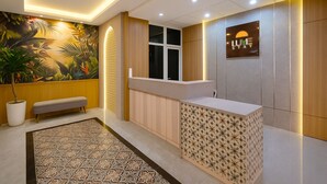 A reception area with a wooden reception desk, a bench, a tropical mural, and a sign that reads "LUME STAY". - Lume Stay by Sinergi (Semarang)