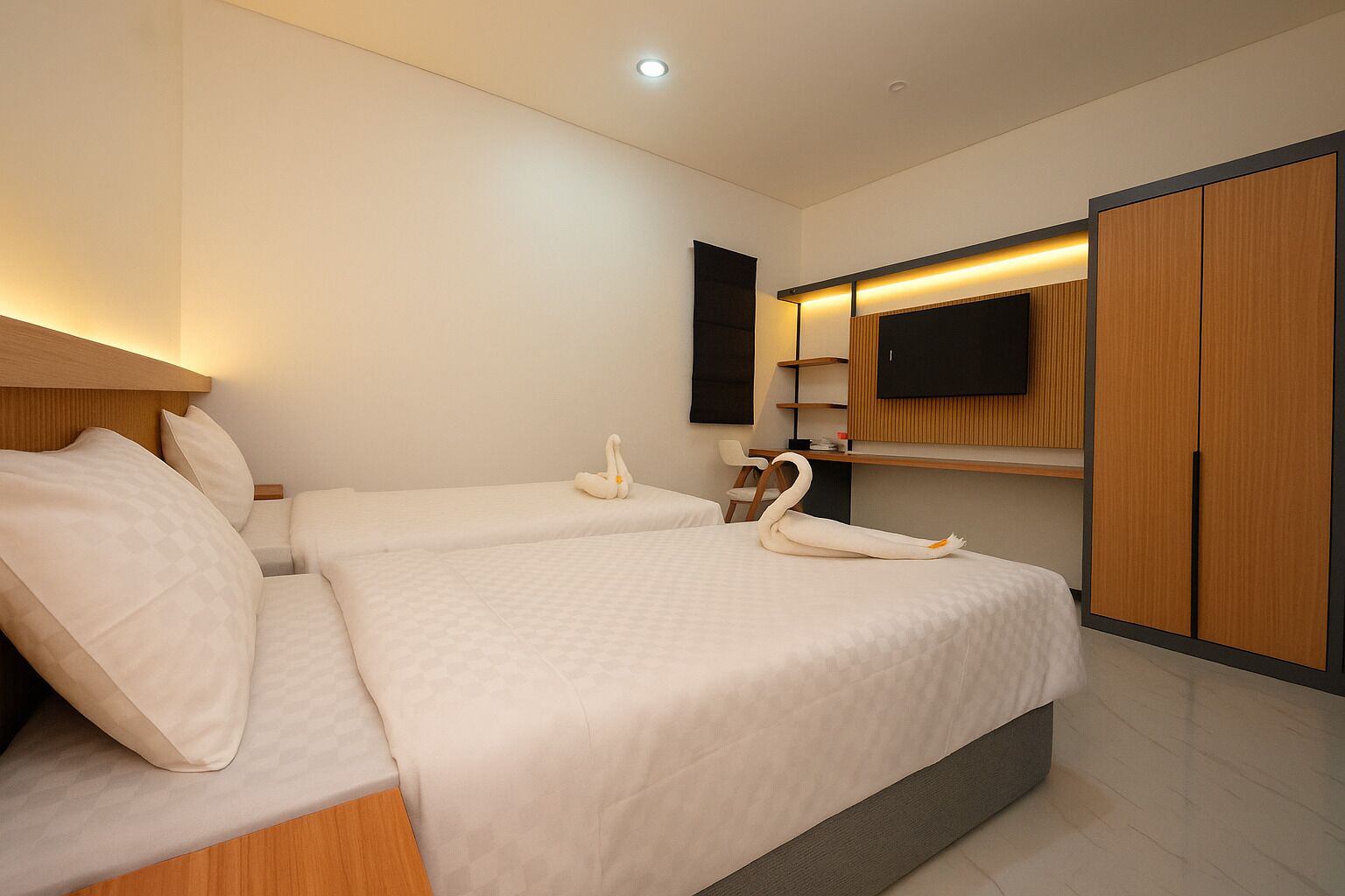 Une chambre d’hôtel avec deux lits, un téléviseur à écran plat fixé au mur, une armoire en bois et un bureau avec une chaise.
