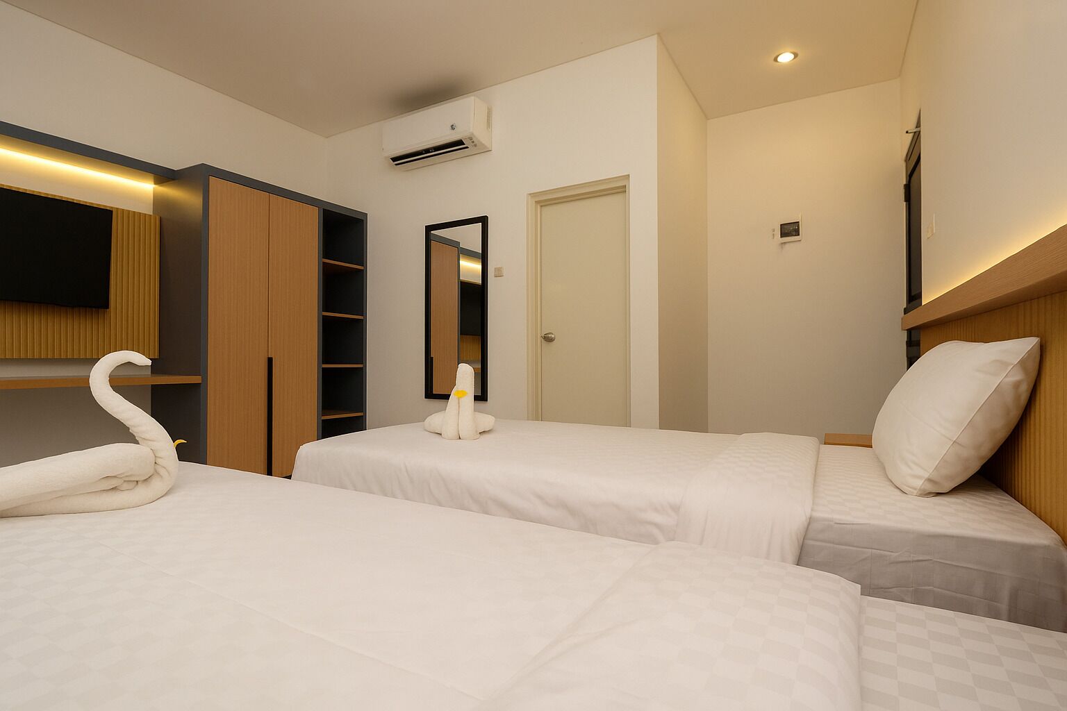 Una habitación de hotel con dos camas, un armario, un espejo y un equipo de aire acondicionado.