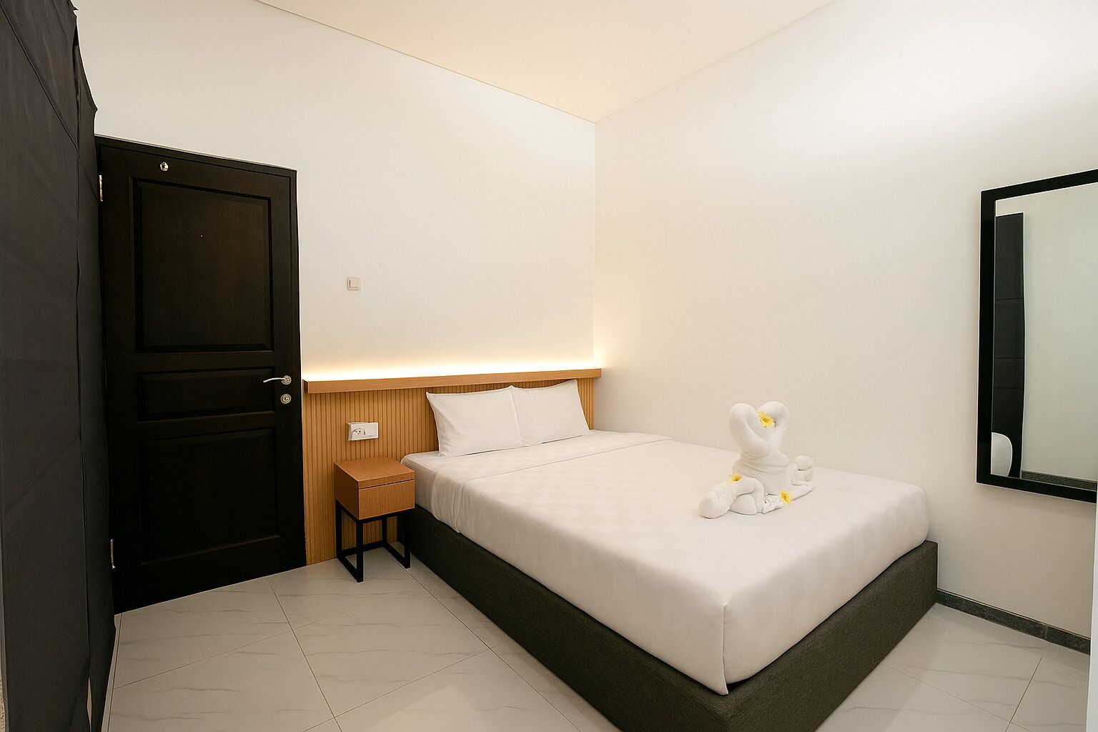 Une chambre d’hôtel avec un lit, une table de chevet, une tête de lit en bois et un miroir au mur.