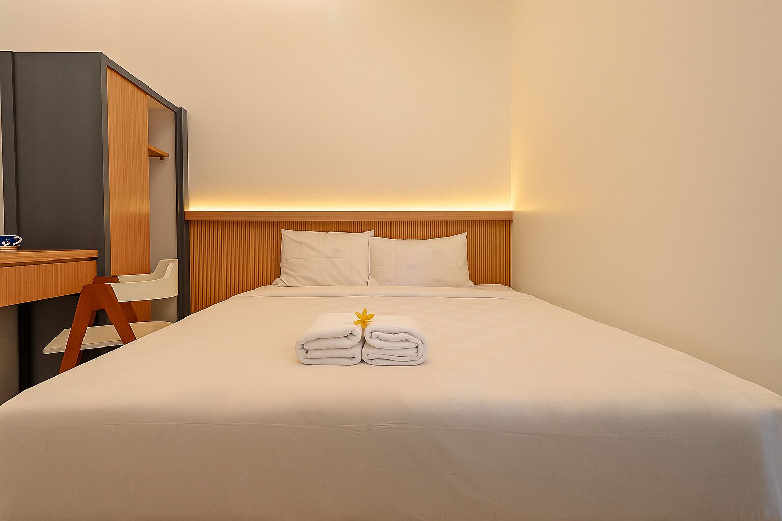 Een eenpersoonsbed met witte lakens, een houten hoofdbord en een nachtkastje met een lamp.