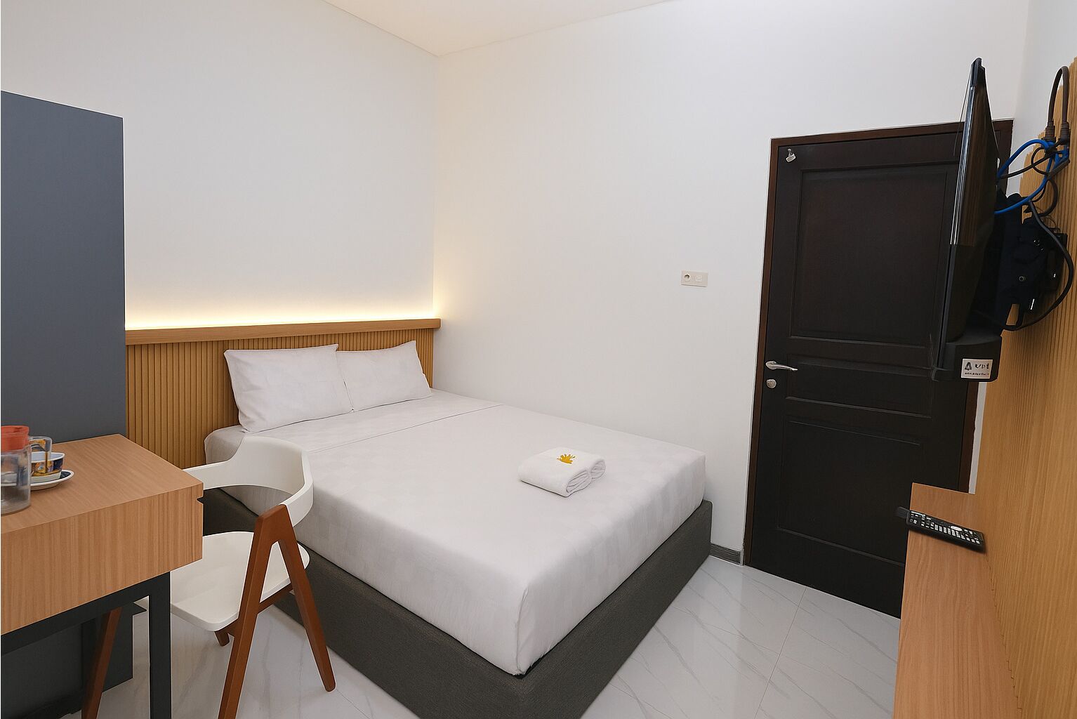 Ein kleines, modernes Hotelzimmer mit einem Einzelbett, einem Schreibtisch und einem Stuhl.