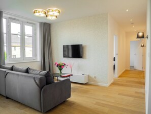 A modern living room with a grey sofa, a flat-screen TV mounted on the wall, and a wooden floor. - Długa 17 Residence (Kraków)
