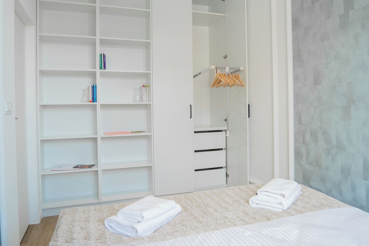 A bedroom with a large white wardrobe, a bed with white linens, and a hanging clothes rack.
