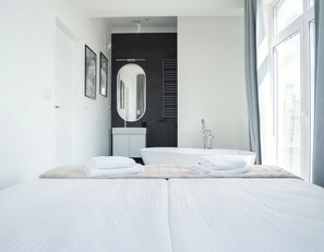 A modern bedroom with a large bed, a bathtub, and a vanity with a mirror. - Długa 17 Residence (Kraków)