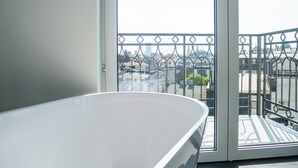 A balcony with a metal railing, a white bathtub, and a view of buildings and a dome in the distance. - Długa 17 Residence (Kraków)