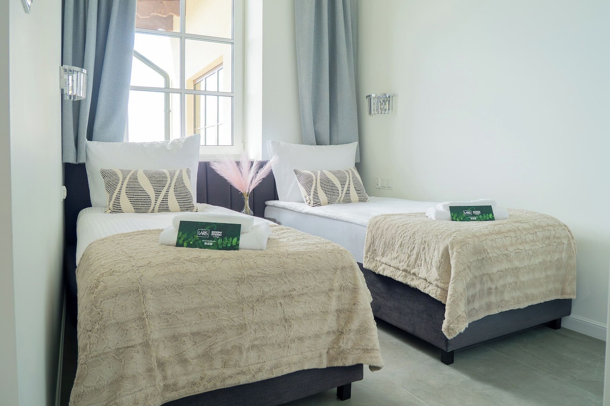 A hotel room with two beds, each with a beige blanket and a LARS brand bottle.